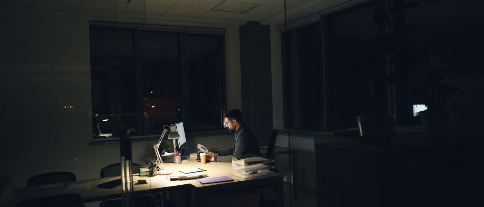 Gece geç saatte ışıkları kapalı ofiste tek başına çalışan kişi